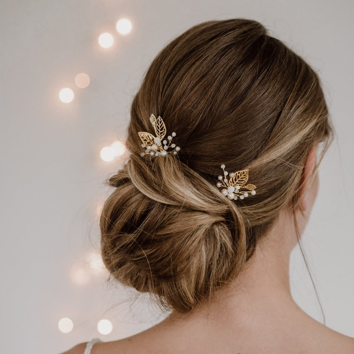 2er Set Braut Haarnadeln Zoe in Gold mit filigranen Blättern, veganen Perlen und white opal Kristallperlen, getragen vom Model in einer Braut Hocksteckfrisur