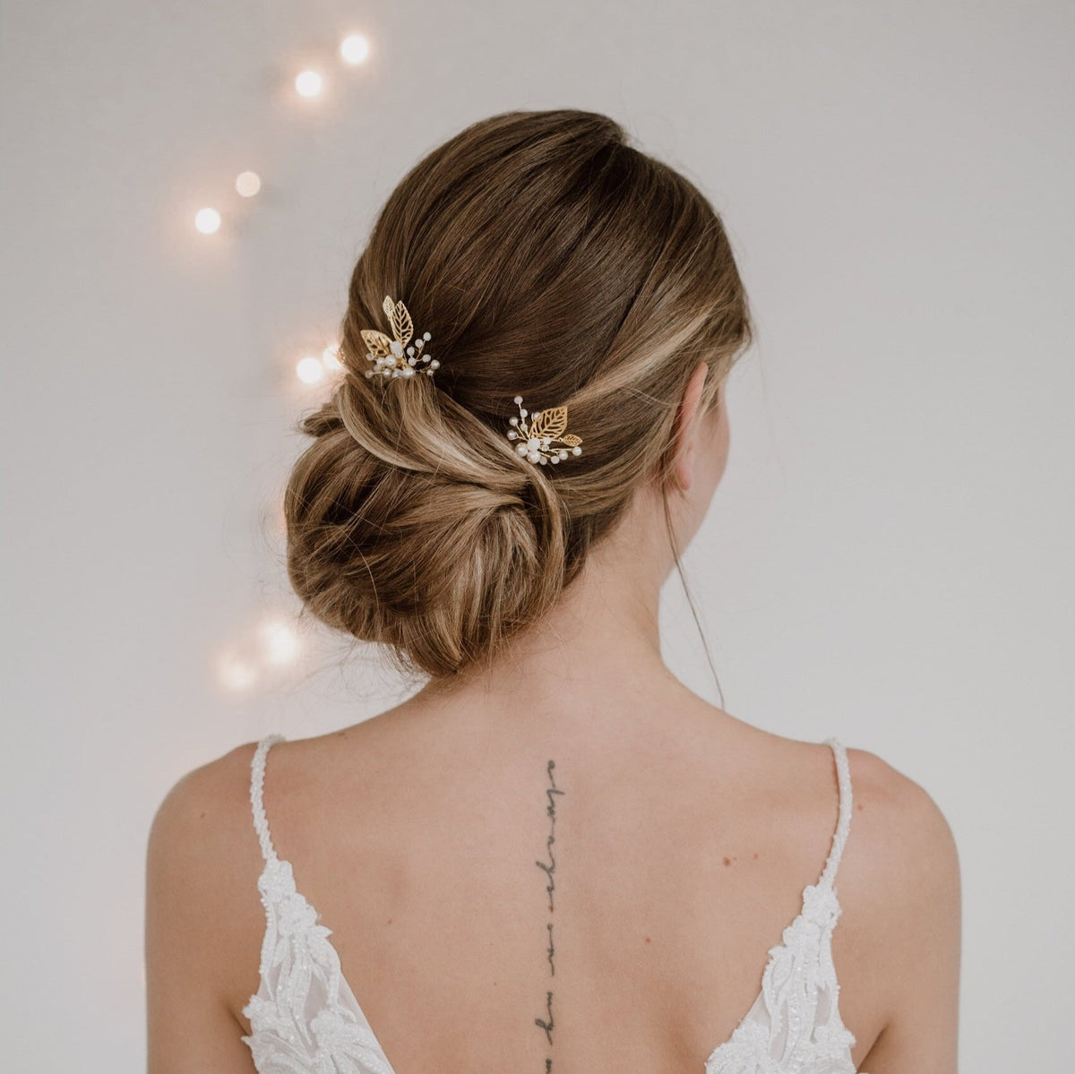 2er Set Braut Haarnadeln Zoe in Gold mit filigranen Blättern, veganen Perlen und white opal Kristallperlen, getragen vom Model in einer Braut Hocksteckfrisur