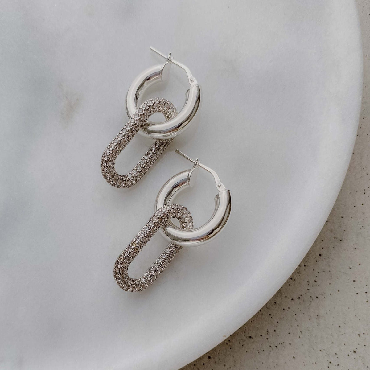 Braut Ohrringe Maxi - Creolen aus 925 Sterlingsilber mit abnehmbarem Zirkonia-Anhänger, liegend auf einer Marmorplatte
