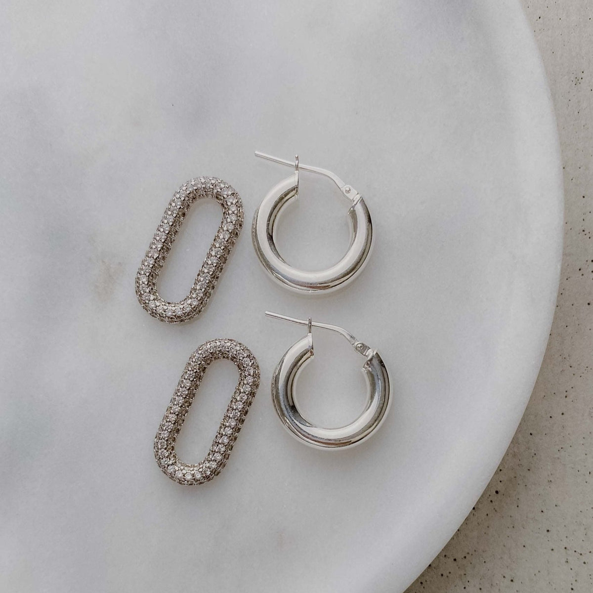 Braut Ohrringe Maxi - Creolen aus 925 Sterlingsilber mit abnehmbarem Zirkonia-Anhänger, liegend auf einer Marmorplatte