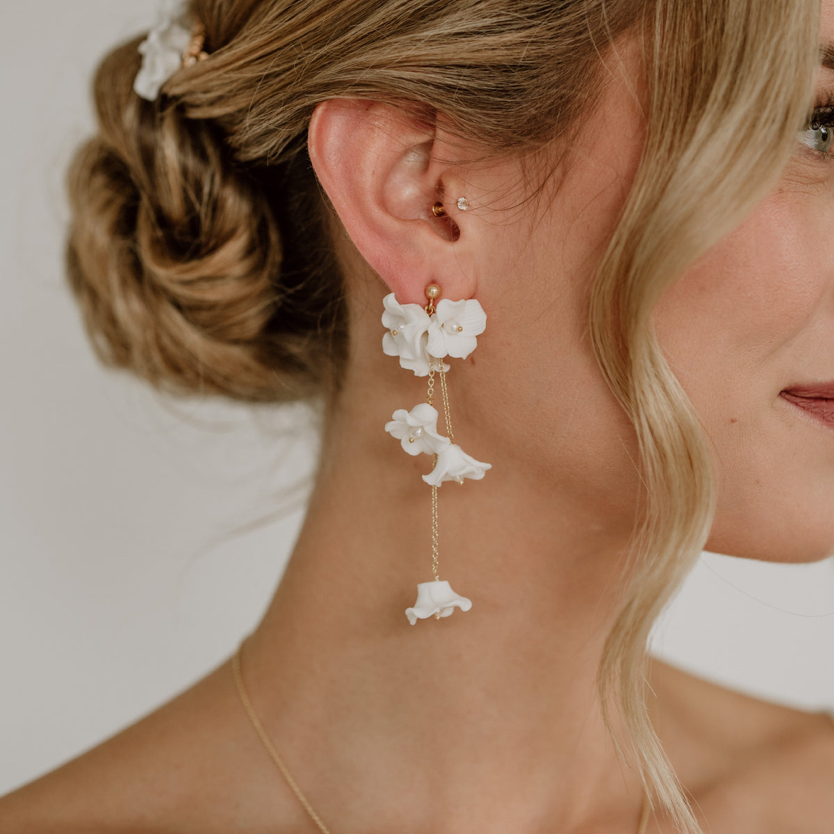 Feine Brautohrringe aus 925er Sterlingsilber 18K vergoldet mit zarten, hängenden Porzellanblüten, elegant getragen von einem Model am Ohr und harmonisch kombiniert mit einer romantischen Brautfrisur.