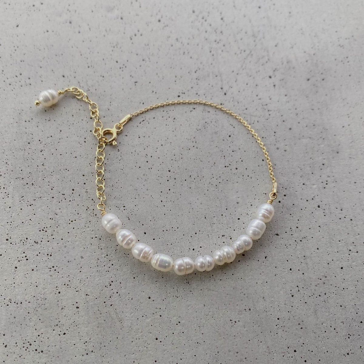 Braut Armband Linn aus 925 Sterlingsilber 18K vergoldet mit echten Süßwasserperlen, Detailaufnahme liegend auf einer Betonplatte