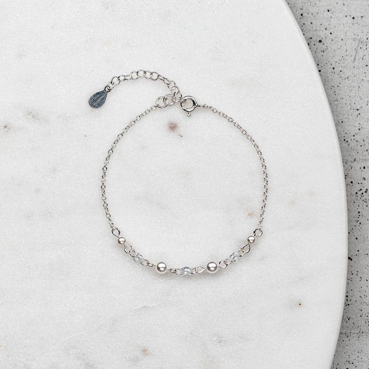 Brautarmband Amina aus 925 Sterlingsilber mit veganen Perlen und Zirkonia Kristallen im Wechsel, verstellbar mit Verlängerungskettchen, liegend auf Marmorplatte