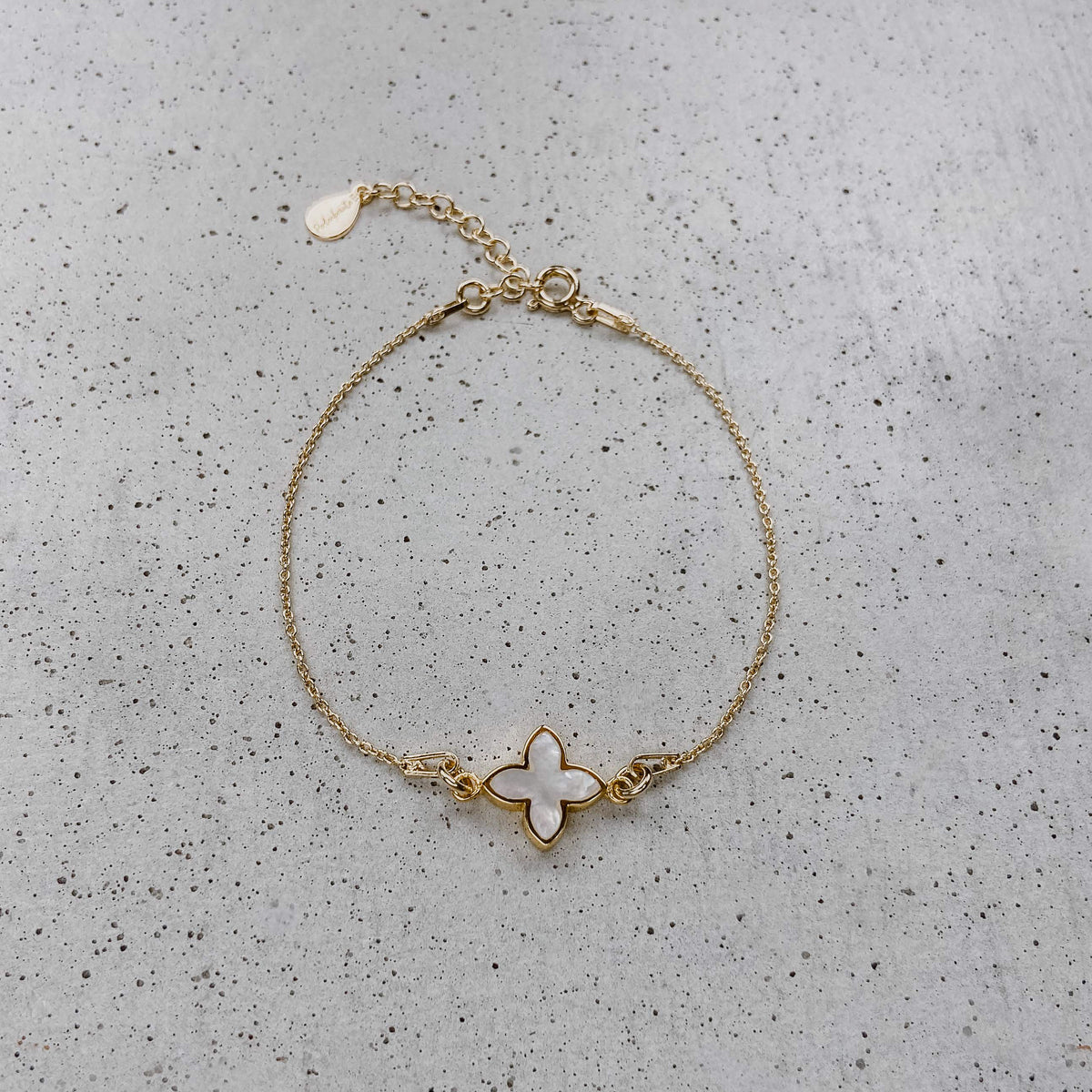 Brautarmband Daisy aus 925 Sterlingsilber 18K vergoldet mit kleiner perlmuttfarbener Blüte, liegend auf einer Betonplatte