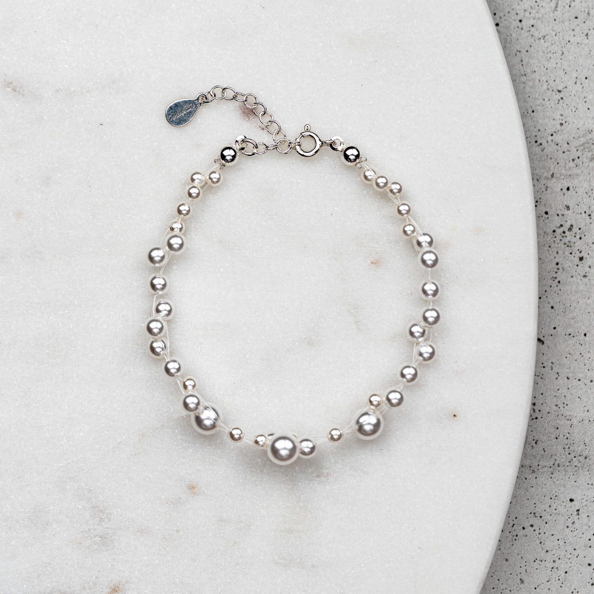 Brautarmband Jasmin mit schwebenden veganen Perlen unterschiedlicher Größe und 925er Sterlingsilber Verschluss, liegend auf Marmorplatte
