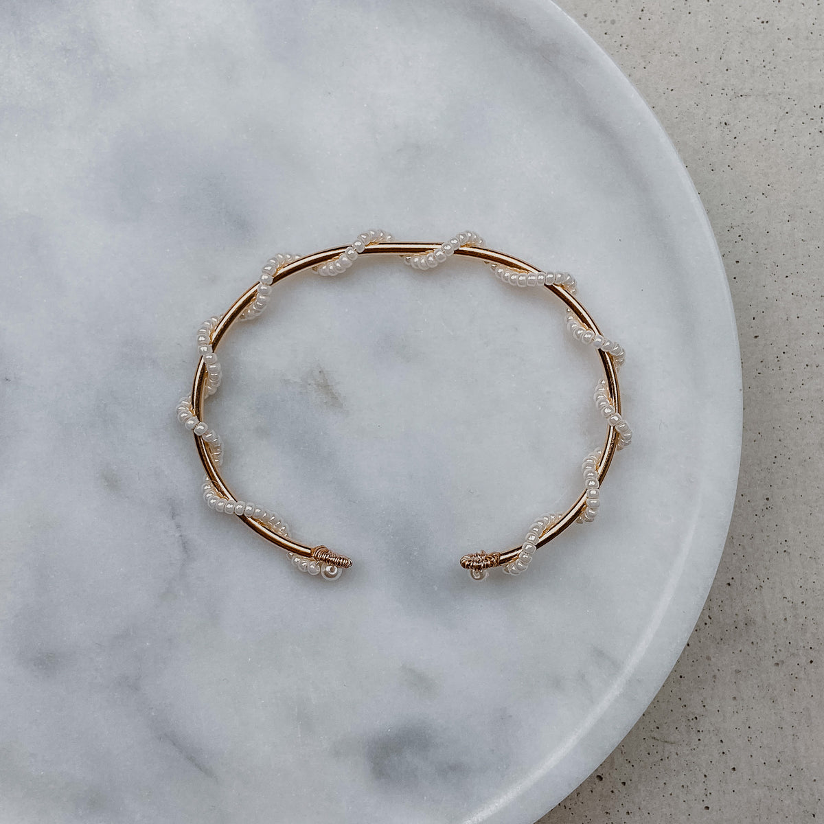 Braut Armreif Belina aus 925 Sterlingsilber 18K rosévergoldet mit kleinen Perlen, gewickelt um einen zarten Armreif, liegend auf Marmorplatte