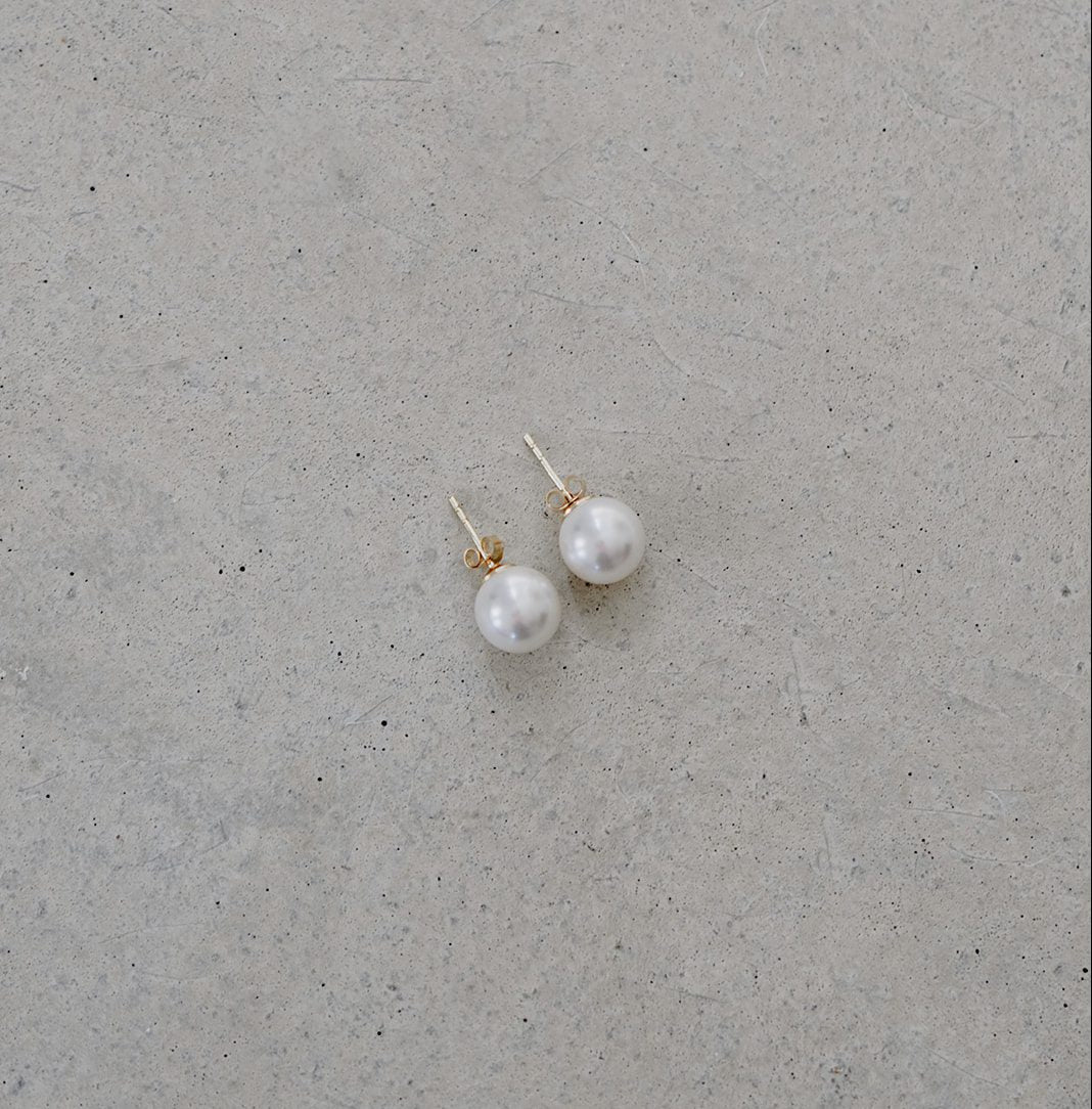 Braut Ohrstecker Perla aus 925 Sterlingsilber 18K vergoldet mit runder weißer 8mm Perle, liegend auf Betonplatte