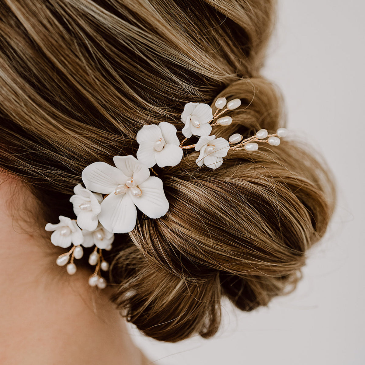 Braut Haarkamm Coco in Gold mit weißen Porzellanblüten und echten Süßwasserperlen, getragen in einer eleganten Hochsteckfrisur