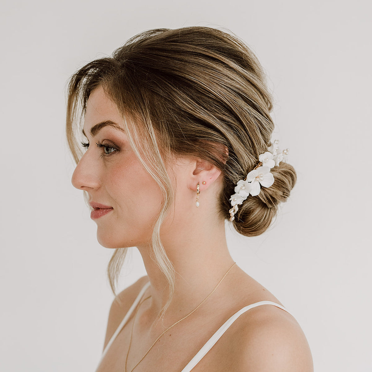 Braut Haarkamm Coco in Gold mit weißen Porzellanblüten und echten Süßwasserperlen mit passenden Creolen Amelie, getragen in einer eleganten Hochsteckfrisur