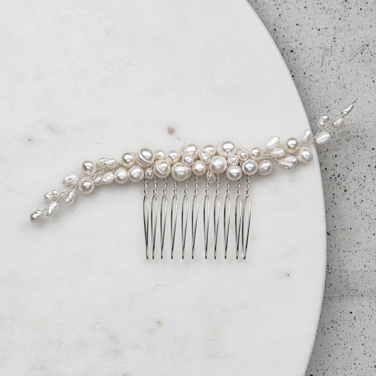 Braut Haarkamm Linda-Amelie in Silber mit unterschiedlich großen, echten Perlen, liegend auf Marmorplatte