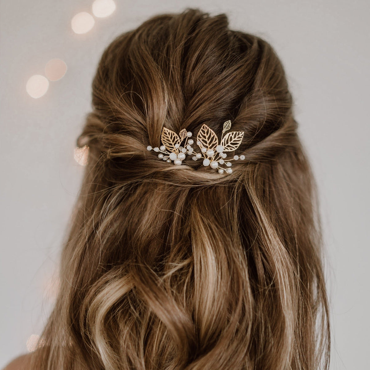 2er Set Braut Haarnadeln Zoe in Gold mit filigranen Blättern, veganen Perlen und white opal Kristallperlen, getragen vom Model in einer halboffenen Brautfrisur in Nahaufnahme
