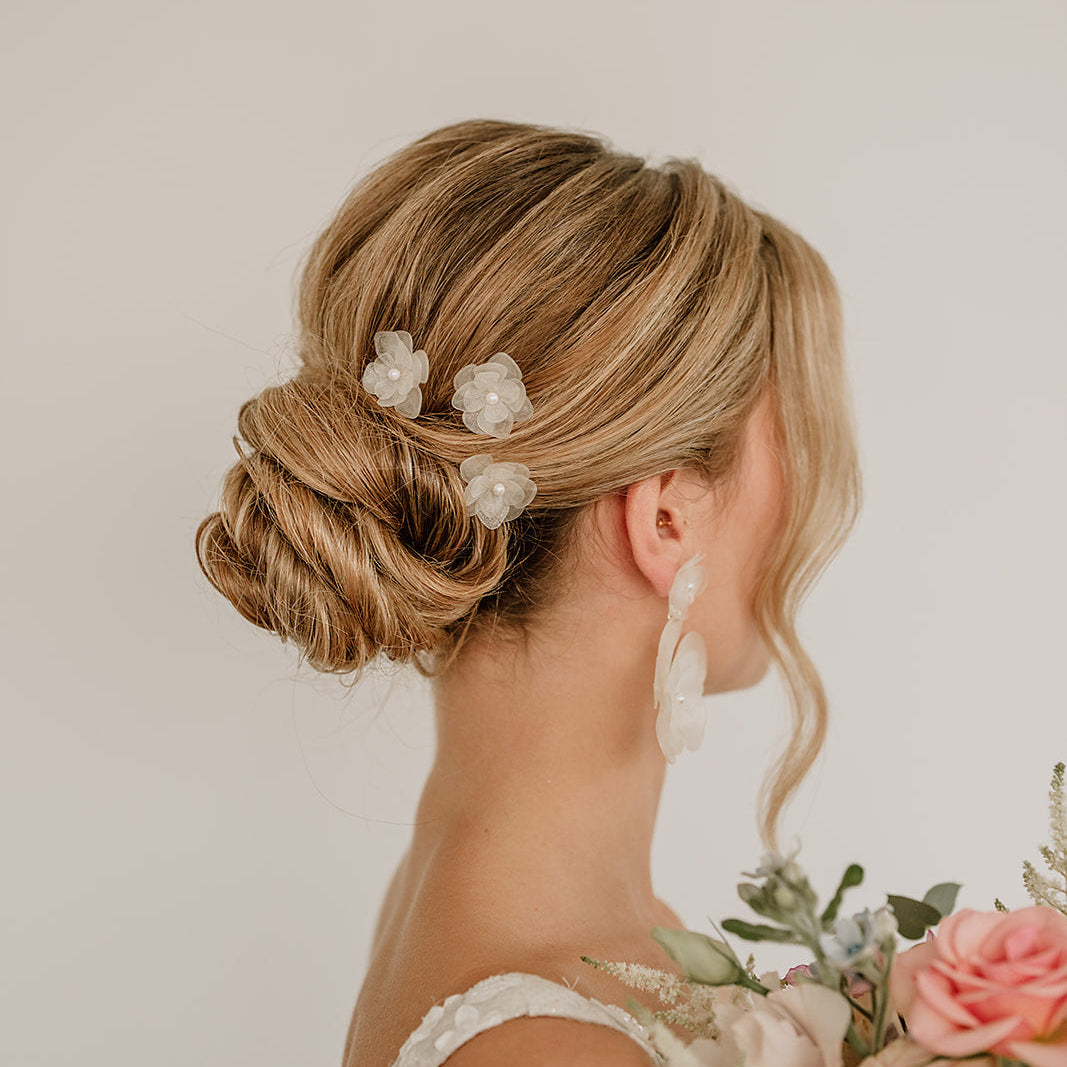 Braut Haarnadeln Carry in Silber mit weißen Blüten aus biobasiertem, nachhaltigen Material und kleinen, veganen Perlen, getragen in einer eleganten Hochsteckfrisur