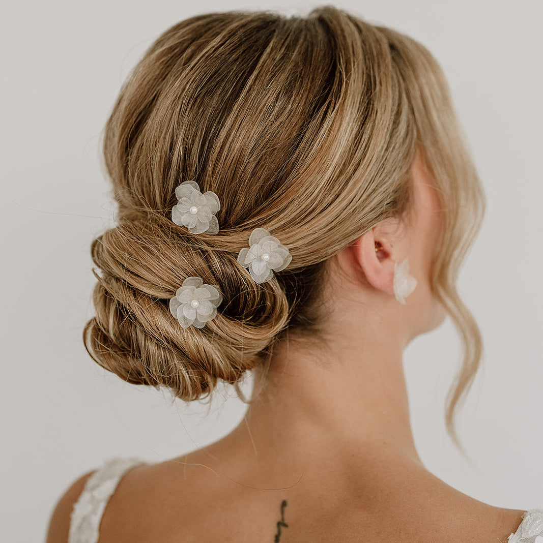 Braut Haarnadeln Carry in Gold mit weißen Blüten aus biobasiertem, nachhaltigen Material und kleinen, veganen Perlen, getragen in einer eleganten Hochsteckfrisur