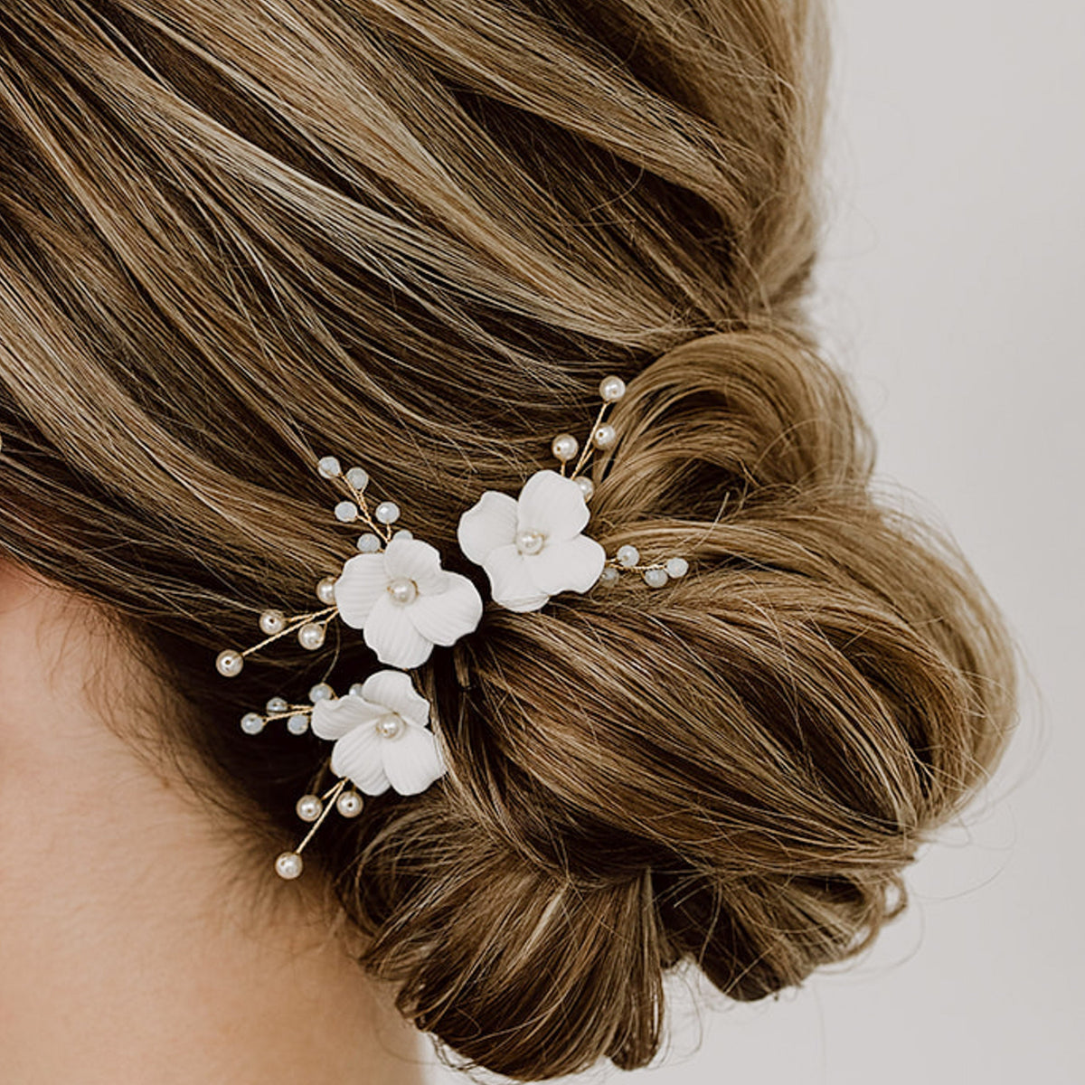 3er Set Braut Haarnadeln Coco mit weißen Porzellan Blüten und veganen Perlen in Gold, getragen von einem Model in einer Brautfrisur
