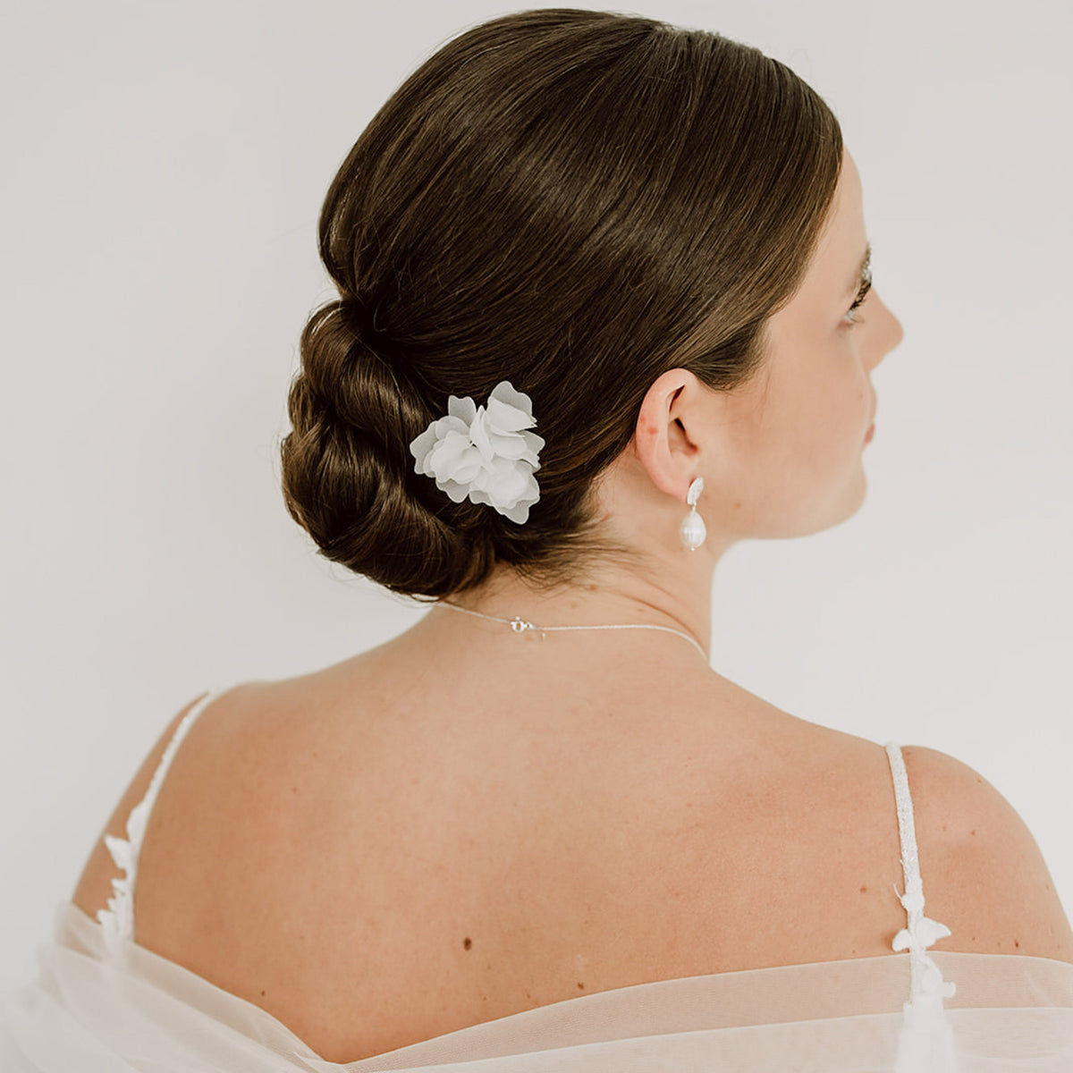 3er Set Braut Haarnadeln Flora in Silber mit weißen Stoffblüten, getragen von einem Model in einer hochgesteckten Brautfrisur