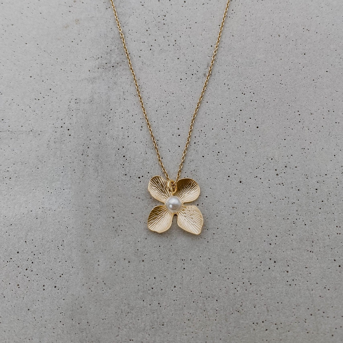 Braut Halskette Victoria aus 925 Sterlingsilber 18K vergoldet mit Blüte und veganer Perle, liegend auf Marmorplatte