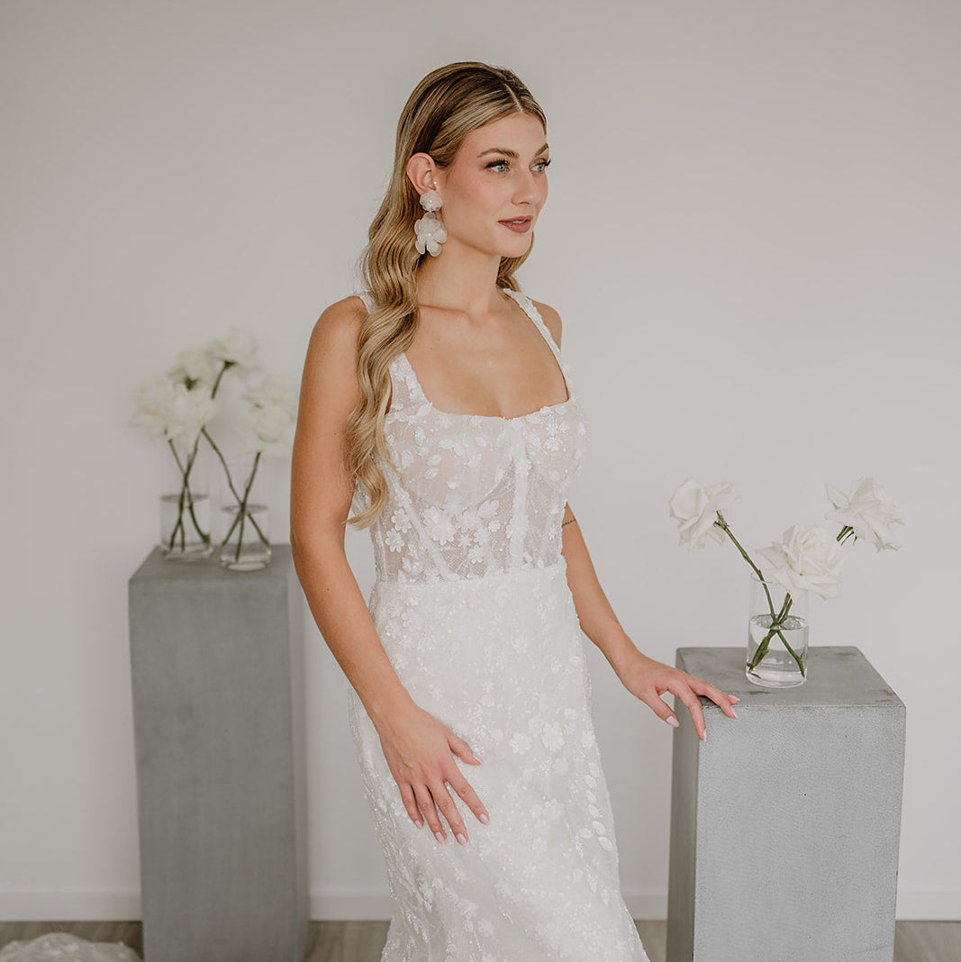 Elegante Statement Brautohrringe aus 925er Sterlingsilber 18K vergoldet mit einer großen und einer kleinen, hängenden Blüte, zu sehen am Model mit spitzen Brautkleid und offenen, gewellten Haaren.