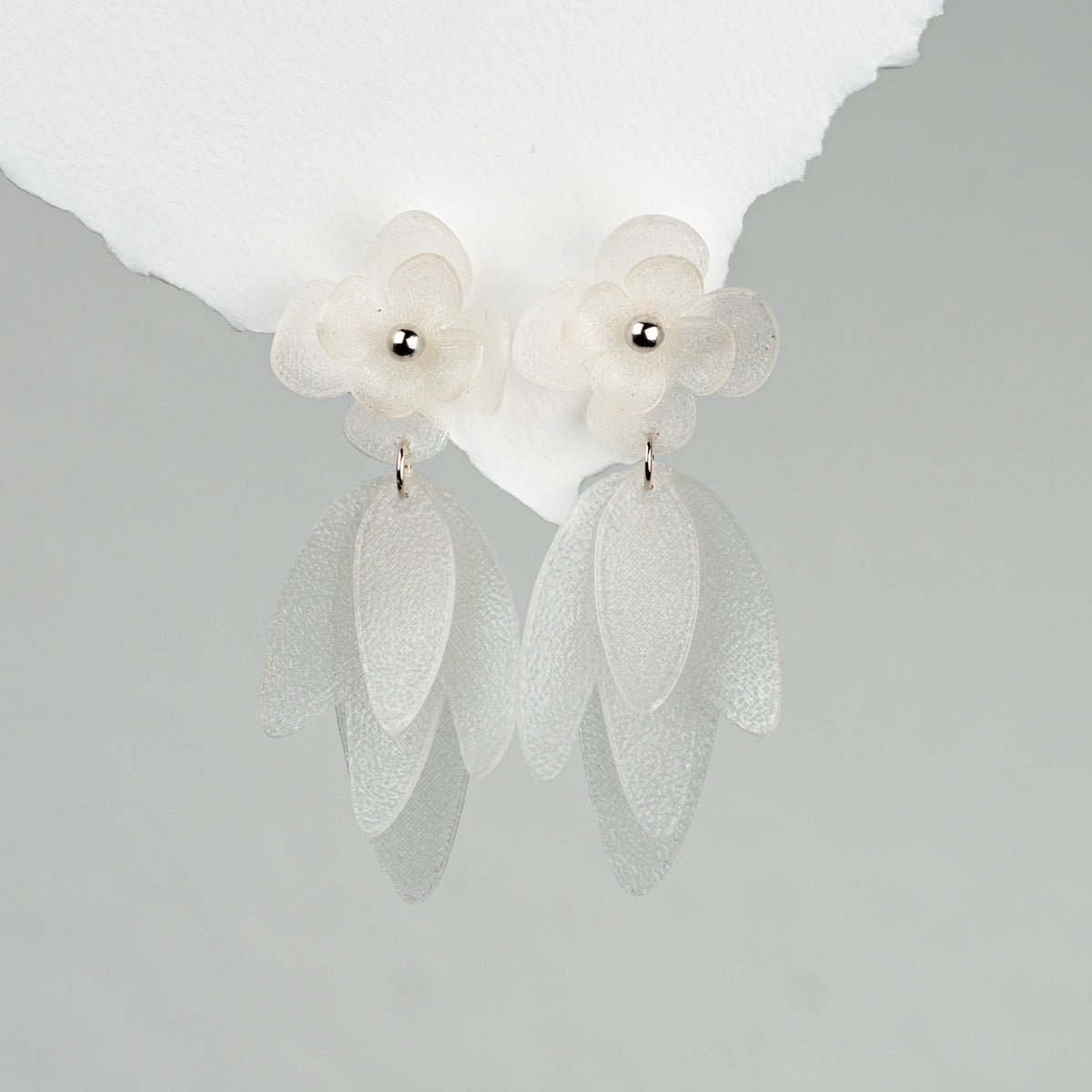 Statement Brautohrringe Chiara mit weißen Blüten aus biobasiertem, nachhaltigen Material, aus 925 Sterlingsilber, liegend auf Marmorplatte