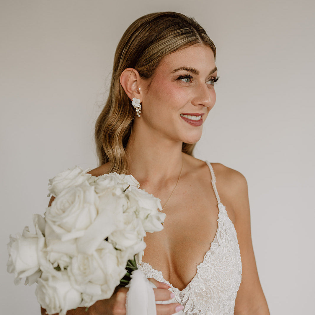 Elegante Brautohrringe aus 925er Sterlingsilber 18K vergoldet mit runder veganer Perle und darunter hängendem, blattförmigem Zirkonia Kristall, stilvoll getragen von einem Model und harmonisch kombiniert mit einer modernen Brautfrisur.