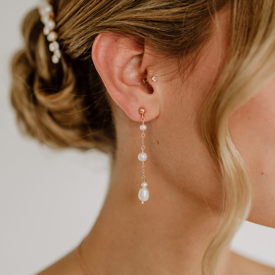 Zarte Brautohrringe aus 925er Sterlingsilber 18K rosévergoldet mit unterschiedlich großen Süßwasserperlen untereinander hängend, elegant getragen von einem Model am Ohr und harmonisch kombiniert mit einer Brautfrisur.