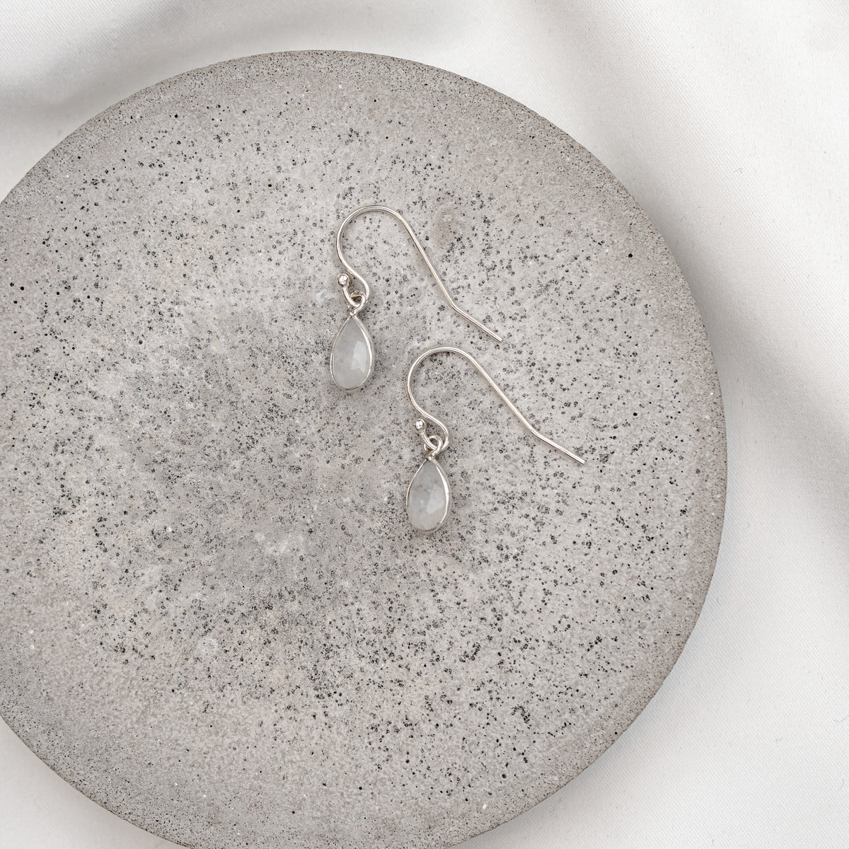 Braut Ohrringe Juna aus 925 Sterlingsilber mit tropfenförmigem Mondstein, liegend auf einer Marmorplatte