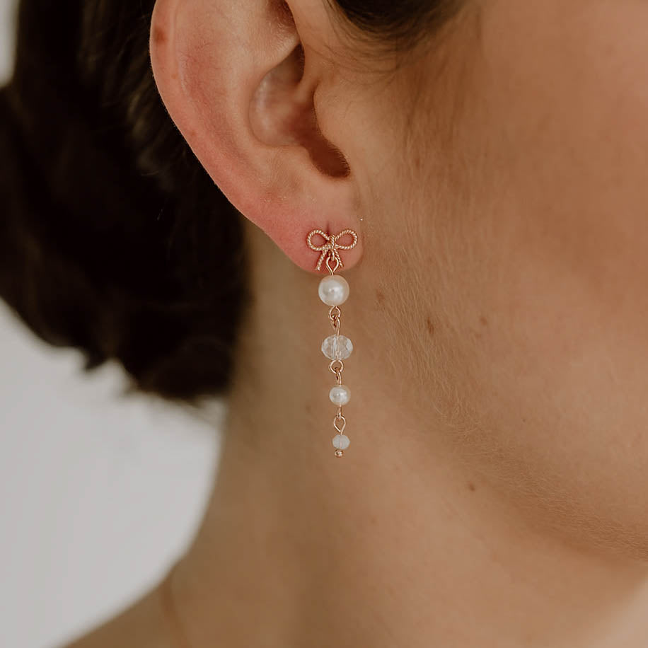 Brautohrringe Pauli mit Schleife aus 925 Sterlingsilber 18K rosévergoldet, darunter hängend Kristallperlen und veganer Perle, am Model getragen in Nahaufnahme