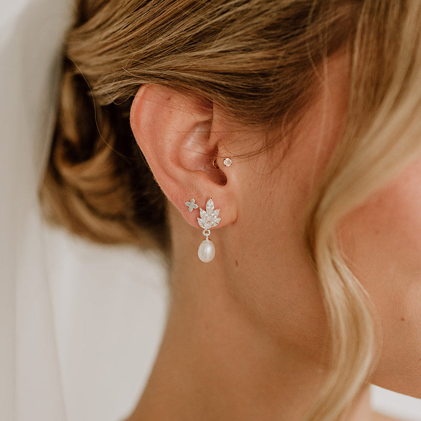 Stilvolle Brautohrringe aus 925er Sterlingsilber 18K vergoldet mit blattförmigen Zirkonia Kristallen und darunter hängender Süßwasserperle, geschmackvoll getragen von einem Model und harmonisch ergänzt durch eine romantische Brautfrisur.