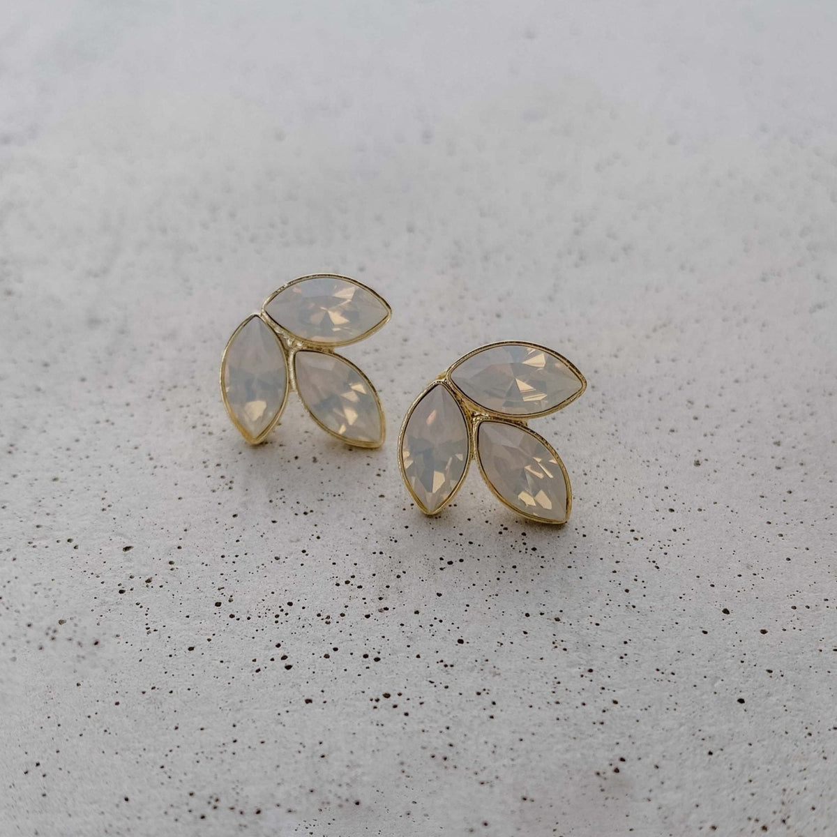 Wunderschöne Brautohrstecker Kate mit funkelnden white opal Kristallen aus 925 Sterlingsilber vergoldet, liegend auf einer Betonplatte