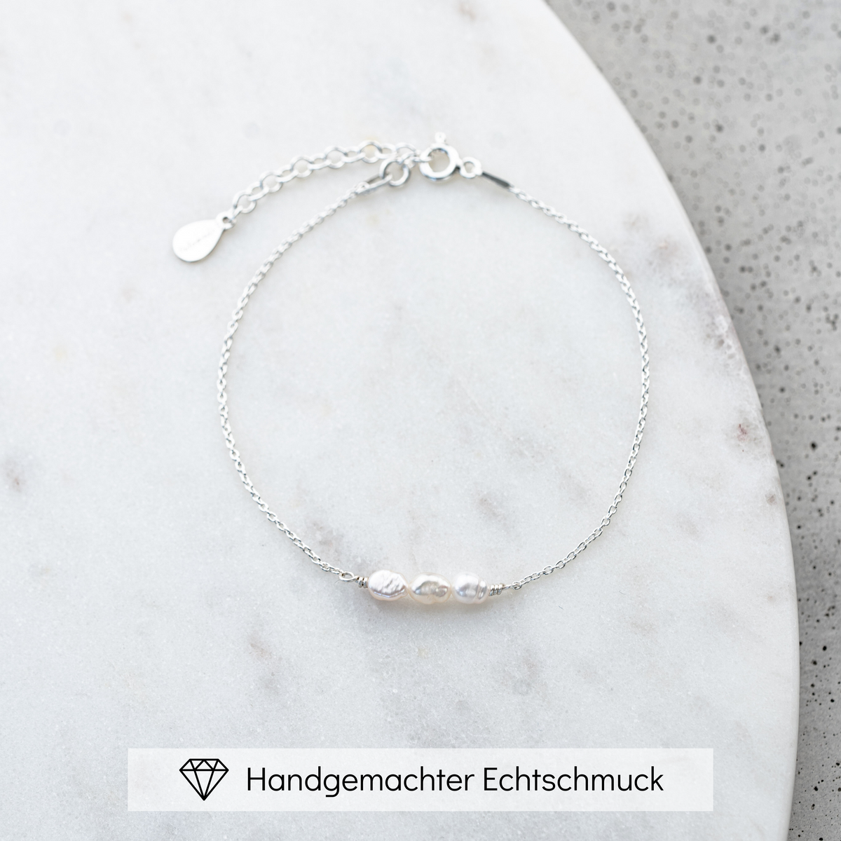 Brautarmband Amelie aus 925 Sterlingsilber mit kleinen echten Süßwasserperlen, liegend auf Marmorplatte