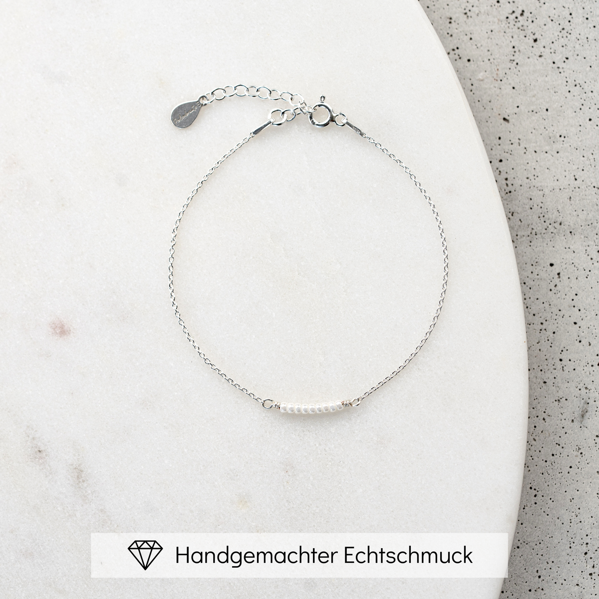 Brautarmband Belina aus 925 Sterlingsilber mit kleinen Perlen, mittig am Armband, liegend auf Marmorplatte