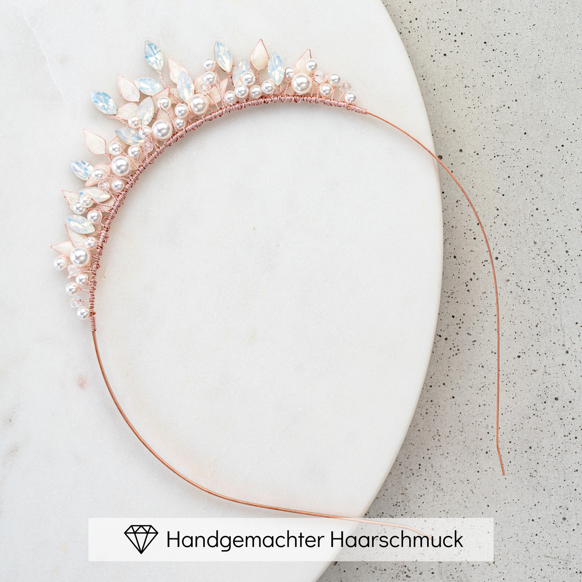 Braut Diadem Krone Greta in Roségold mit veganen Perlen, white opal Kristallen und ivory farbenen Blättern, liegend auf einer Marmorplatte