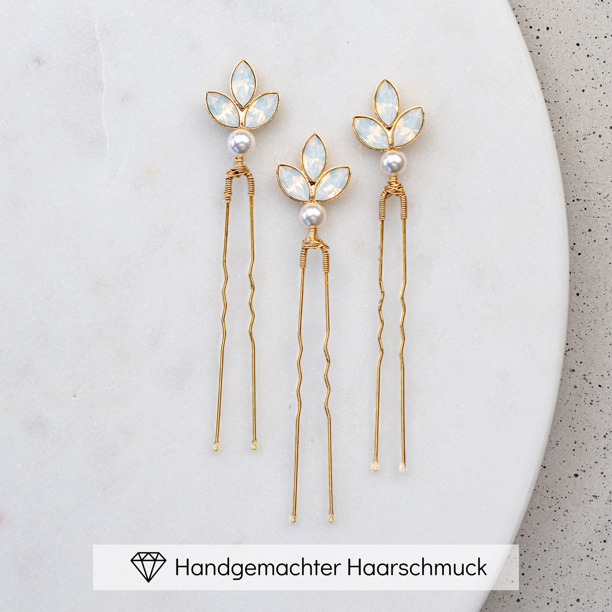 3er Set Haarnadeln Kate in Gold mit white opal Kristallblättern und veganer Perle, liegend auf einer Marmorplatte