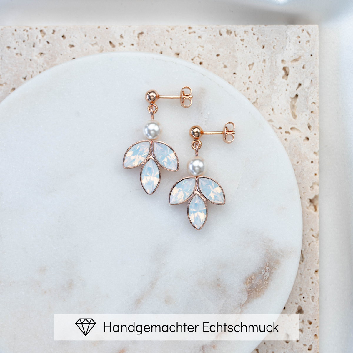 Zarte hängende Brautohrringe aus 925er Sterlingsilber 18K rosévergoldet mit rundem Kugelstecker, kleiner runder veganer Perle und darunter angeordneten blattförmigen, white opal Kristallen, ästhetisch arrangiert auf einer hellen Marmorplatte.