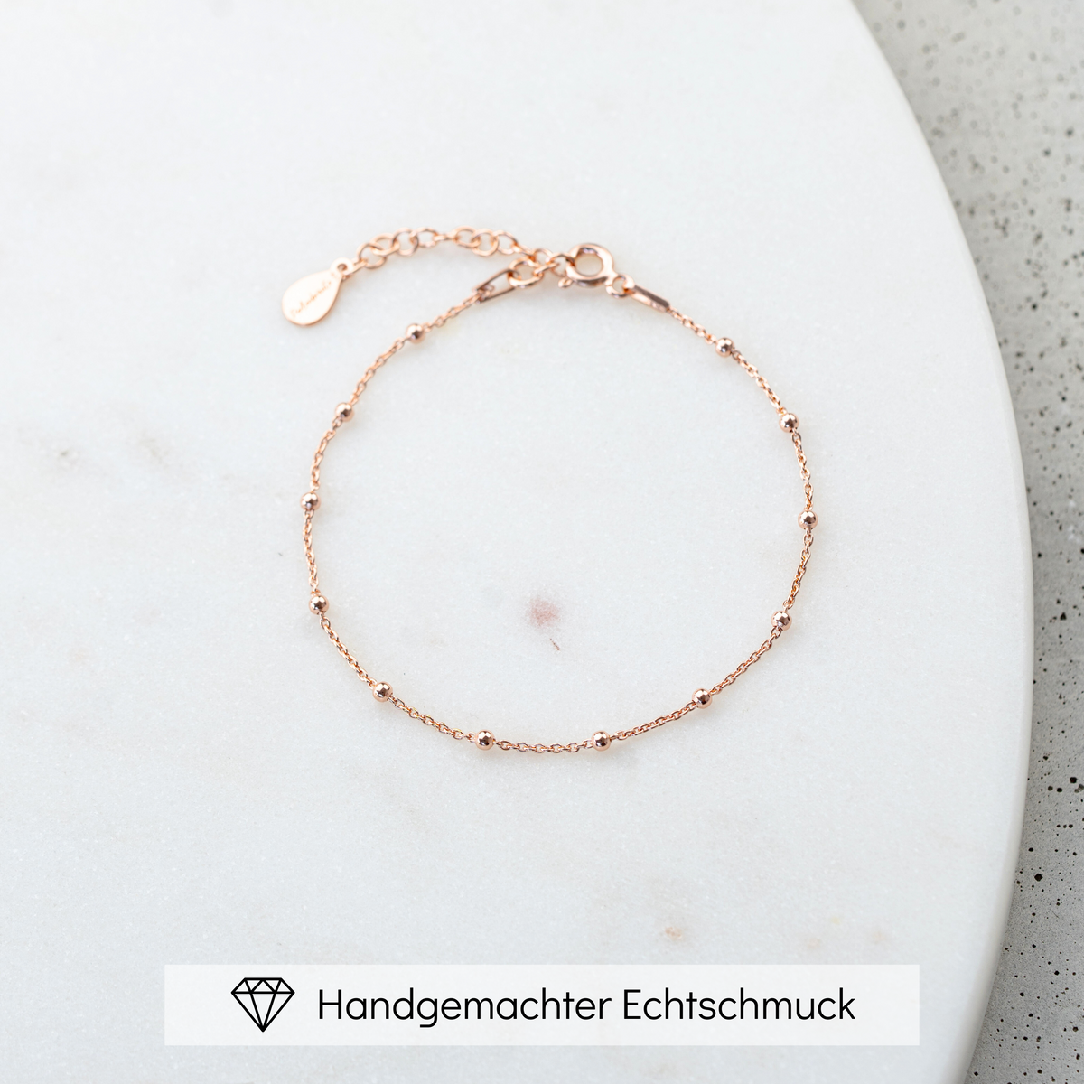 Dezentes Brautarmband Kaya aus 925 Sterlingsilber 18K rosévergoldet mit kleinen Kugeln, liegend auf einer Marmorplatte