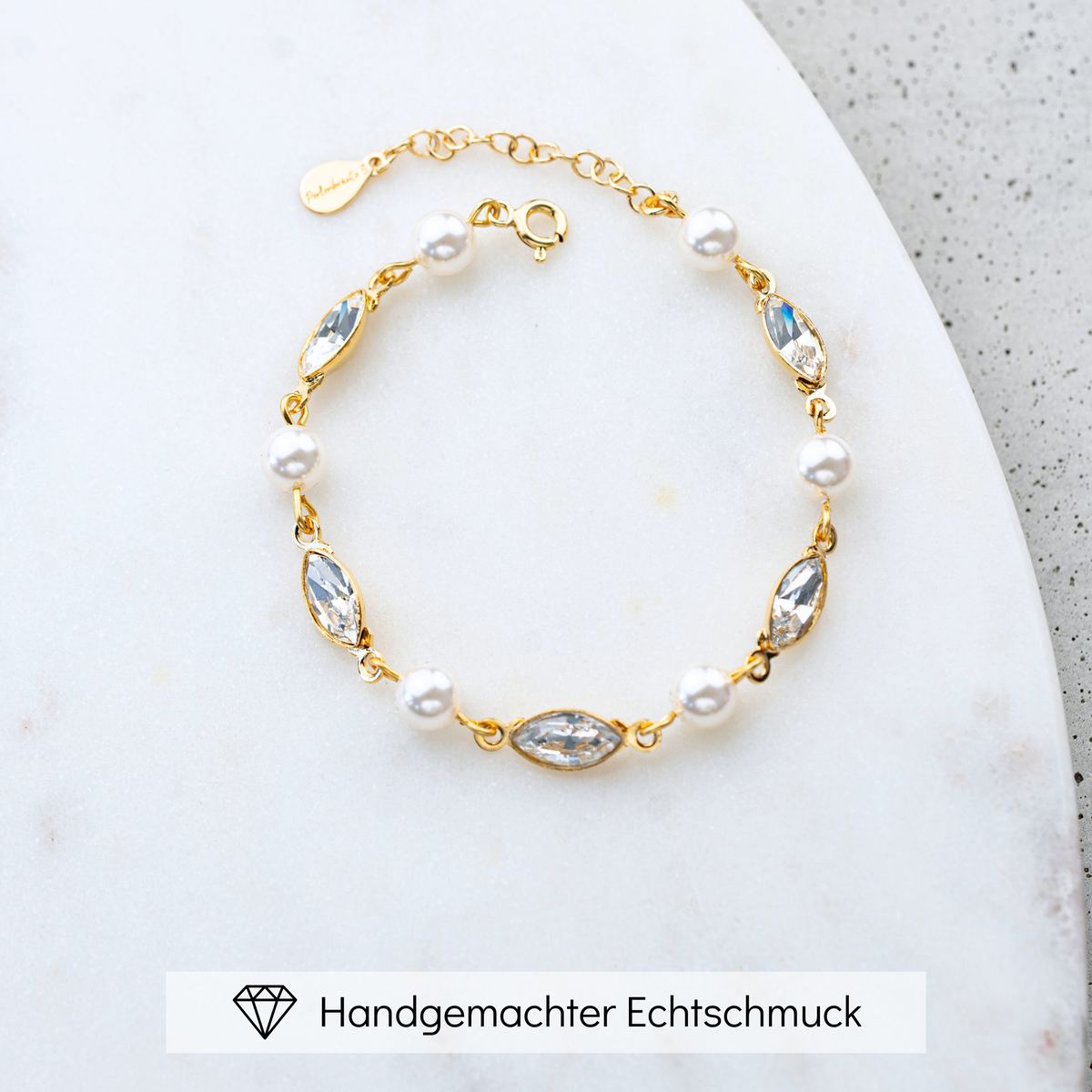 Brautarmband Kylie aus 925 Sterlingsilber 18K vergoldet mit veganen Perlen und crystal Kristallen im Wechsel, liegend auf einer Marmorplatte