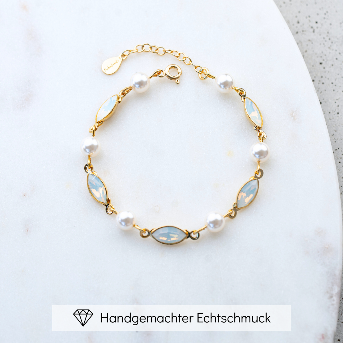 Brautarmband Kylie aus 925 Sterlingsilber 18K vergoldet mit veganen Perlen und white opal Kristallen im Wechsel, liegend auf einer Marmorplatte