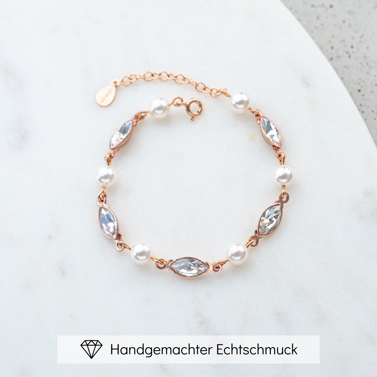 Brautarmband Kylie aus 925 Sterlingsilber 18K rosévergoldet mit veganen Perlen und crystal Kristallen im Wechsel, liegend auf einer Marmorplatte
