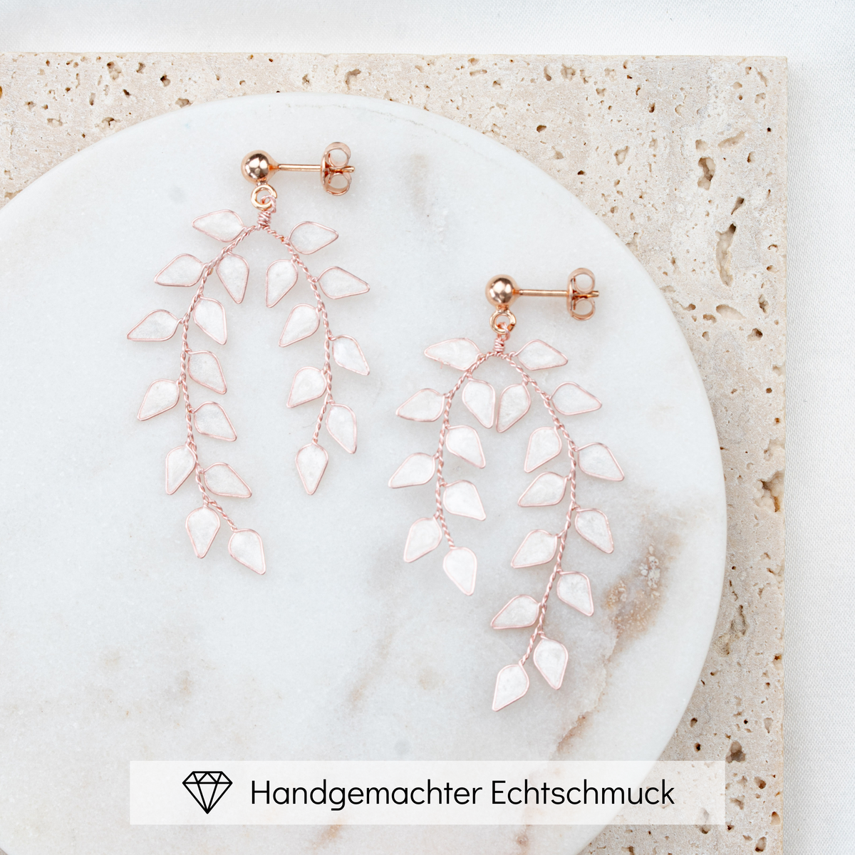 Geschmackvolle Brautohrringe aus 925er Sterlingsilber 18K rosévergoldet mit ivory farbigen, blattförmigen Ranken, liegend und detailreich auf einer Marmorplatte dargestellt.