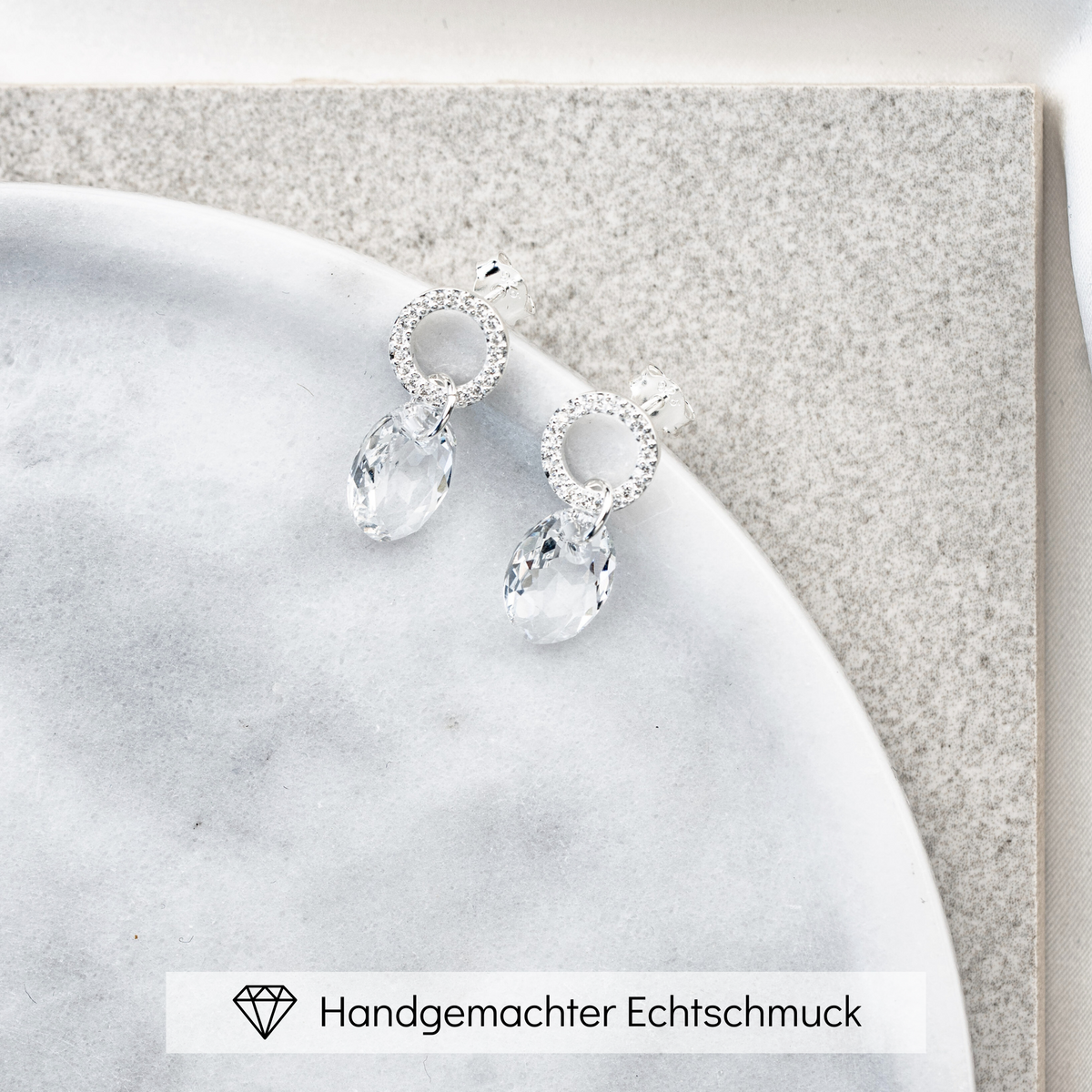 Hängender Braut Ohrring Mimi aus 925 Sterlingsilber mit Zirkonia Kristallen und facettiertem Kristall, liegend auf einer Marmorplatte