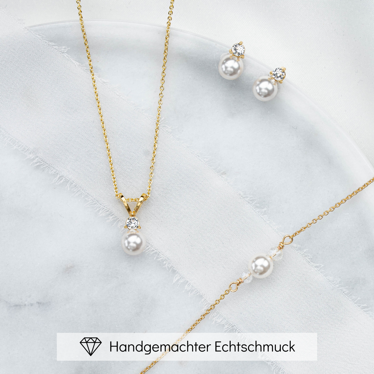 Hochwertiges Brautschmuck-Set aus 925er Sterlingsilber 18K vergoldet bestehend aus Brauthalskette, Ohrsteckern und Armband mit funkelndem Zirkonia Kristall und veganer Perle, ästhetisch arrangiert auf einer hellen Marmorplatte.