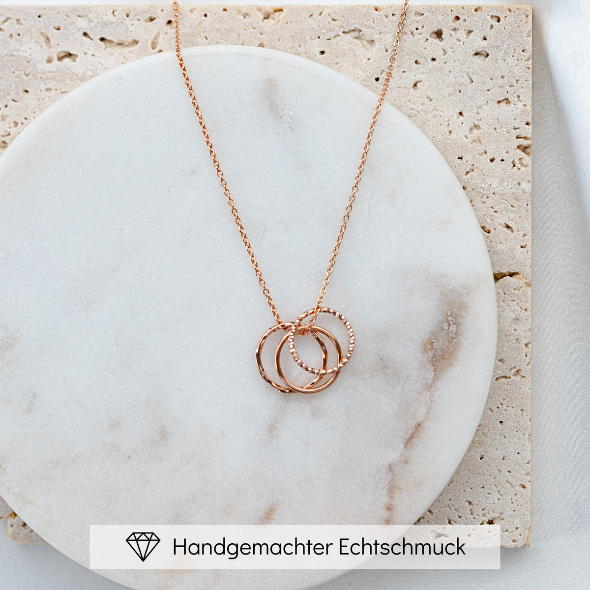 Brautkette Toni Trio aus 925 Sterlingsilber 18K rosévergoldet mit drei ineinander verschlungenen, unterschiedlich gemusterten Ringen, liegend auf Marmorplatte