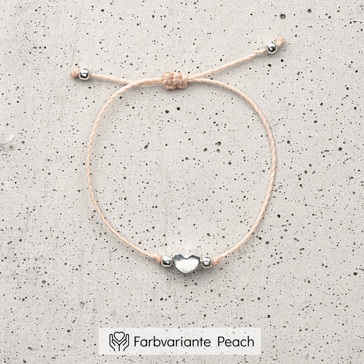 Trauzeugin Armband aus pfirsichfarbenem Makramee-Band mit silbernem Herz-Bead, liegend auf Marmorplatte