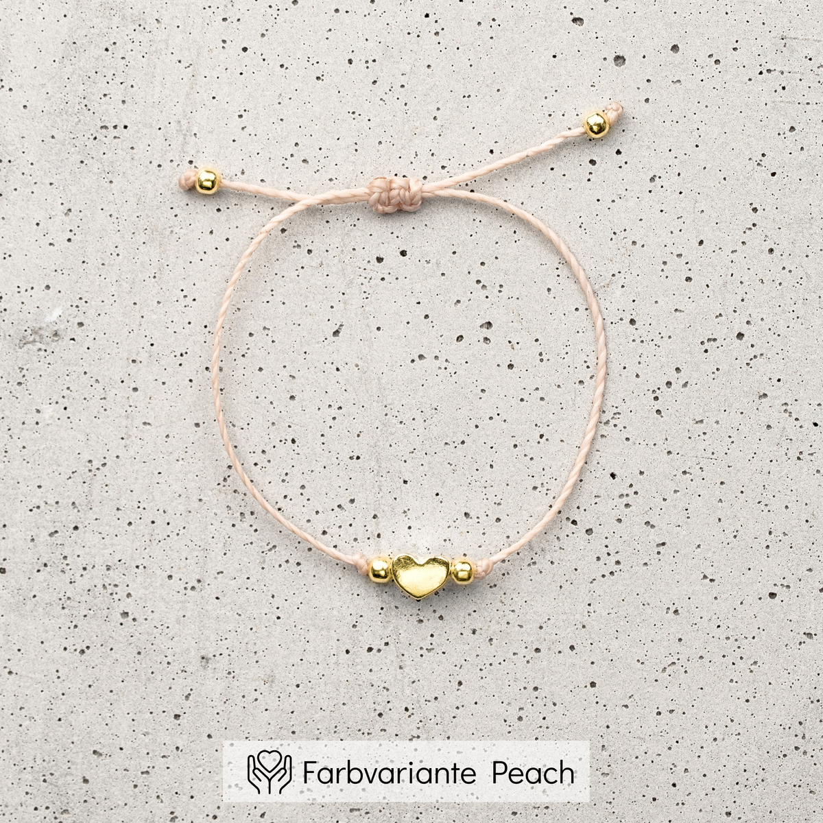 Trauzeugin Armband aus pfirsichfarbenem Makramee-Band mit goldenem Herz-Bead, liegend auf einer Betonplatte