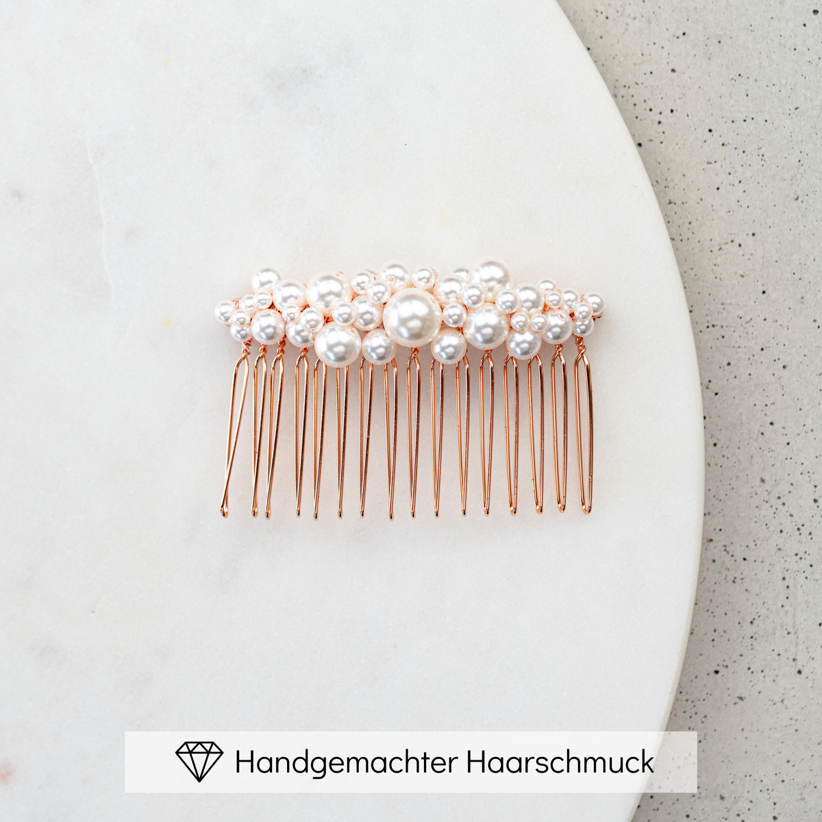 Braut Haarkamm Wilma in Roségold mit unterschiedlich großen, veganen Perlen, liegend auf einer Marmorplatte