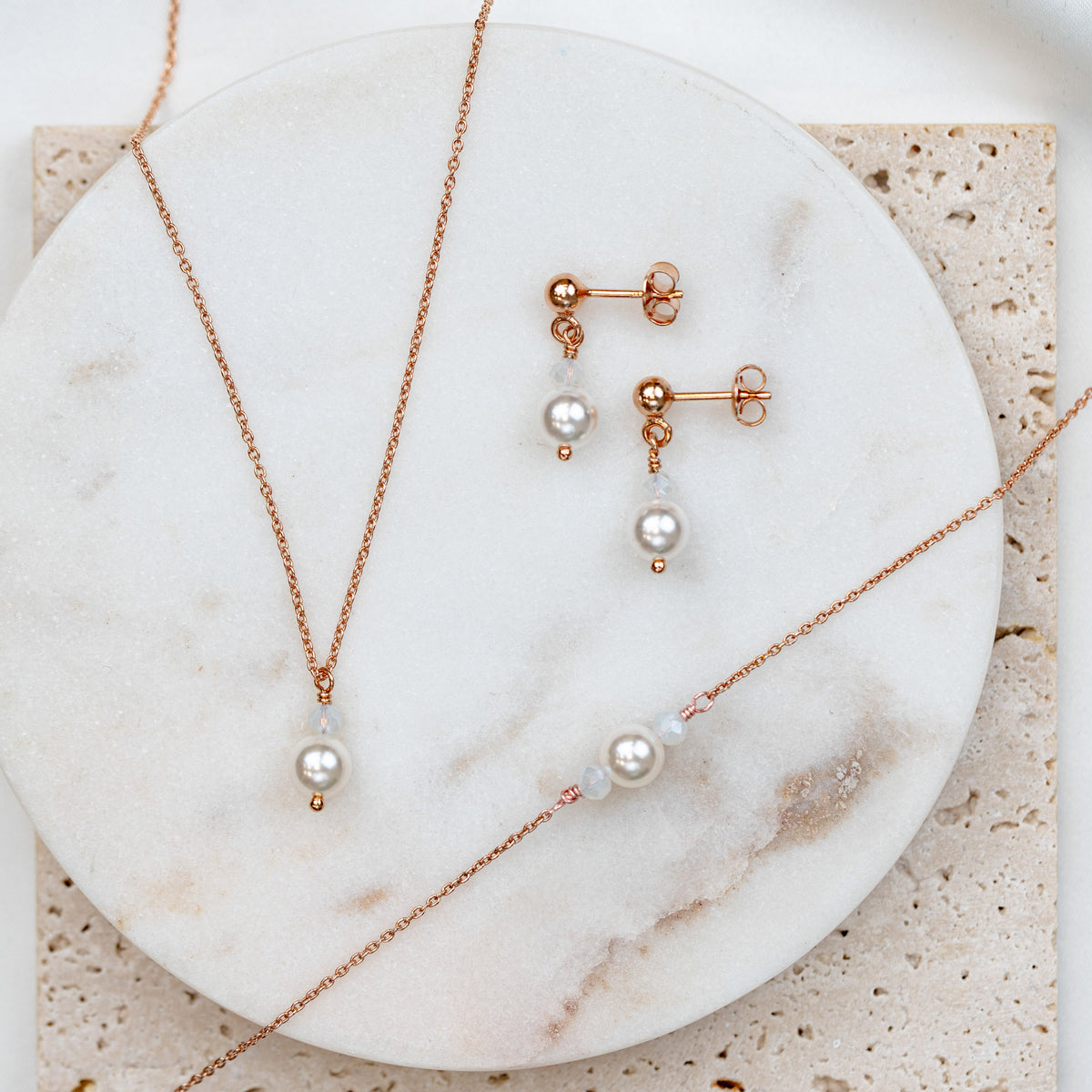3-teiliges Brautschmuckset Ari aus 925 Sterlingsilber 18K rosévergoldet – Ohrringe, Halskette und Armband mit veganen Perlen und Kristallperlen white opal, auf Marmorplatte