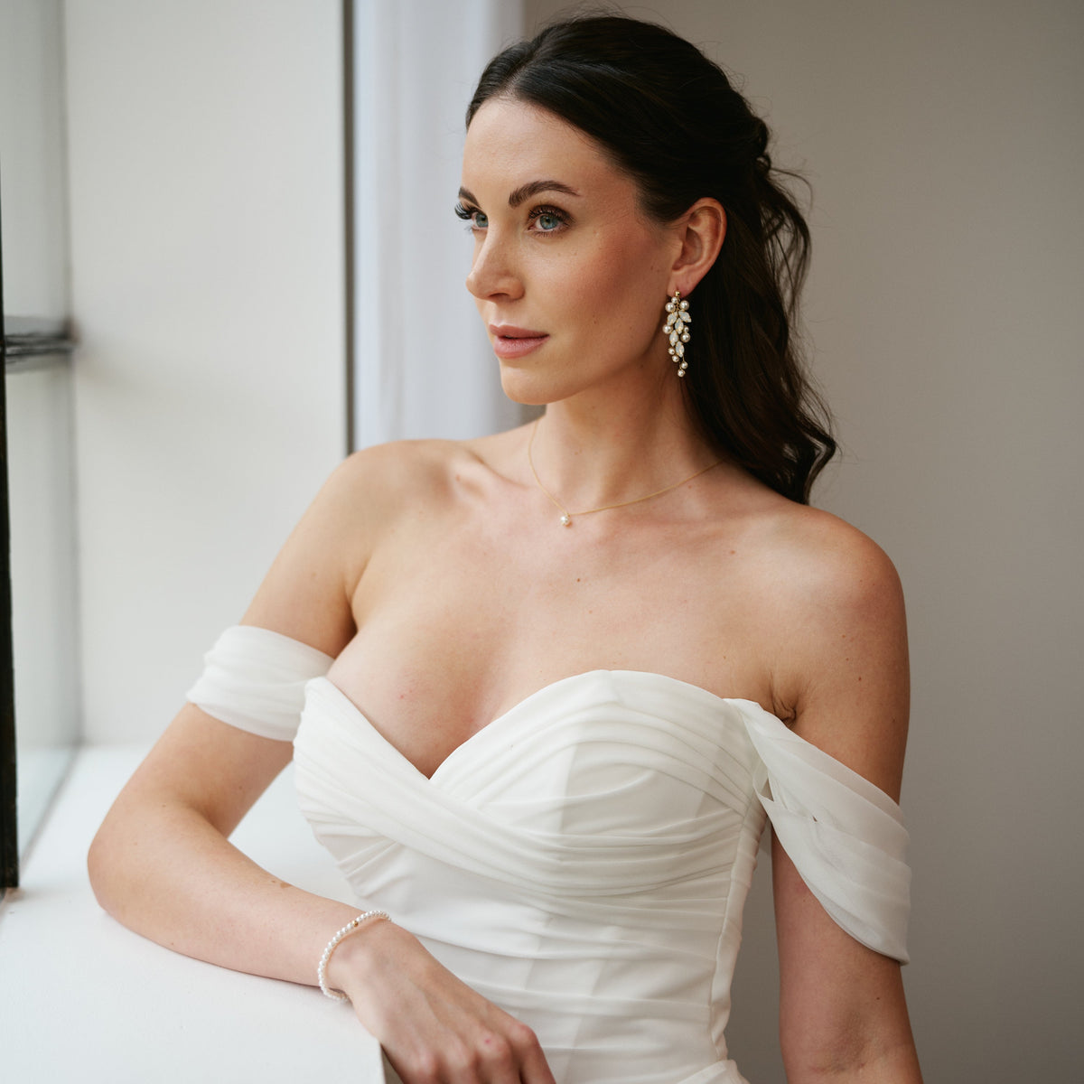 Model trägt Braut Ohrringe Anastasia, Braut Halskette Perla und Braut Perlenarmband Perla mit halboffenen Haaren und schulterfreiem Brautkleid