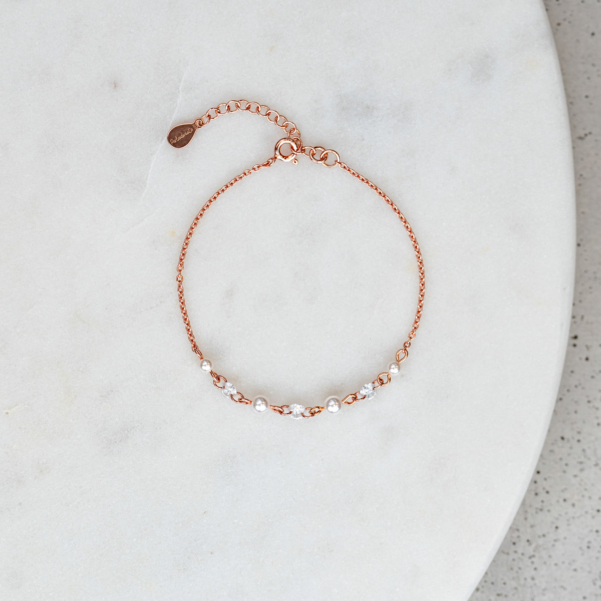 Brautarmband Amina aus 925 Sterlingsilber 18K rosévergoldet mit veganen Perlen und Zirkonia Kristallen im Wechsel, verstellbar mit Verlängerungskettchen, liegend auf Marmorplatte