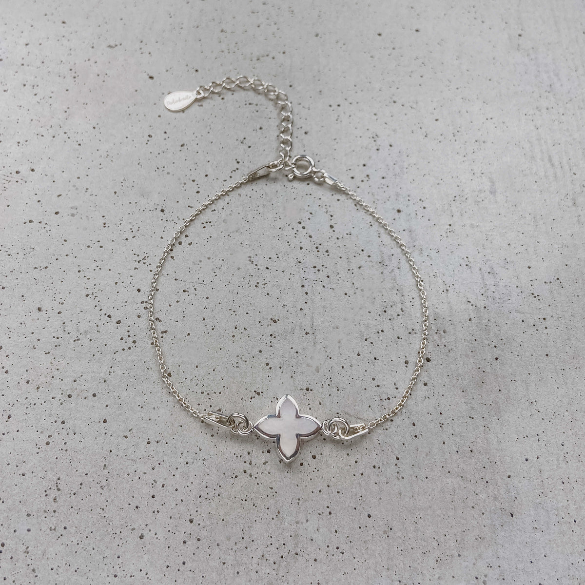 Brautarmband Daisy aus 925 Sterlingsilber mit kleiner perlmuttfarbener Blüte, liegend auf einer Betonplatte