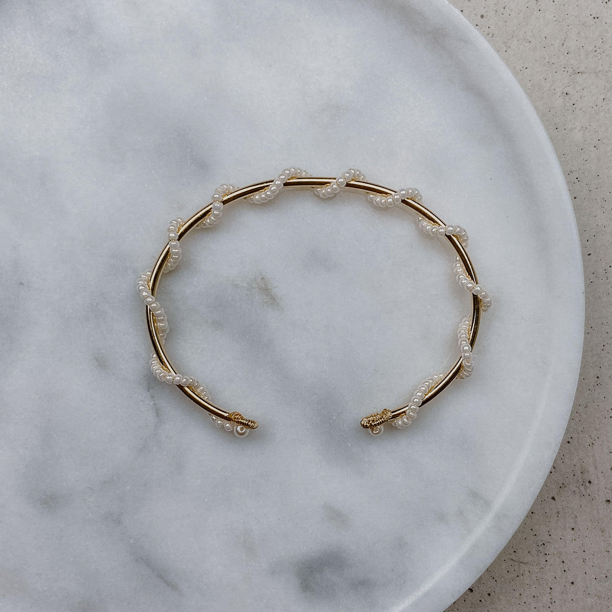 Braut Armreif Belina aus 925 Sterlingsilber 18K vergoldet mit kleinen Perlen, gewickelt um einen zarten Armreif, liegend auf einer Marmorplatte