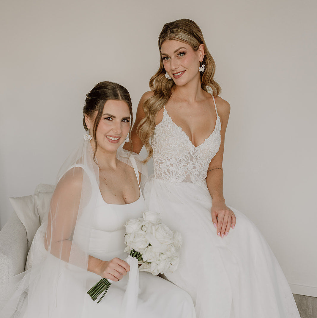 Elegante Brautohrringe aus 925er Sterlingsilber 18K vergoldet mit filigranen Porzellanblüten und kleinen Süßwasserperlen an einer feinen, runden Creole, stilvoll getragen von zwei Models und harmonisch kombiniert mit klassischen Brautkleidern und romantischen Brautfrisuren.